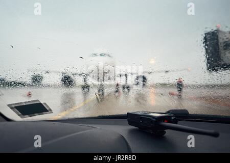 Ein geschäftiger Flughafen im Regen. Ein Blick durch eine nasse Fenster im Flugzeug vor dem Flug. Stockfoto