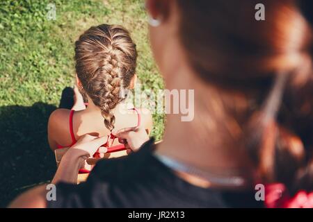 Junge Frau Haarflechten des kleinen Mädchens auf dem Garten auf dem Lande machen. Stockfoto