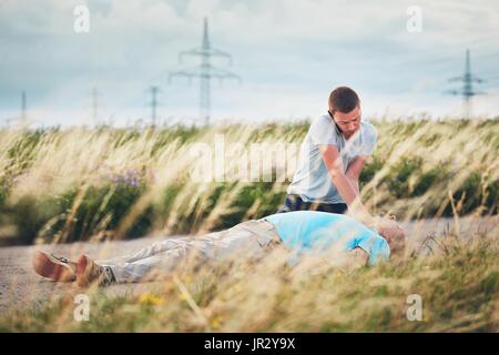 Junger Mann für Rettungsdienst anrufen. Dramatische Reanimation auf der Landstraße. Themen zu retten, Hilfe und Hoffnung. Stockfoto