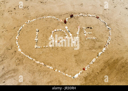 Wort Liebe und Herz Form hergestellt aus Kieselsteinen am Sandstrand Stockfoto