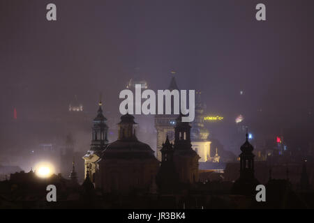 Nacht Nebel über Sankt-Nikolaus Kirche (Kostel Svatého Mikuláše) und das Altstädter Rathaus (Staroměstská Radnice) am Altstädter Ring in Prag, Tschechien. Die Kuppel des Nationalmuseum (Národní Muzeum) ist im Hintergrund zu sehen. Stockfoto