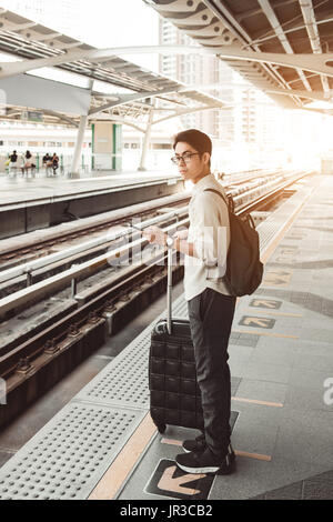 Mann ist auf dem Bahnhof mit Reisetasche, mit Handy, warten auf einen Zug Stockfoto