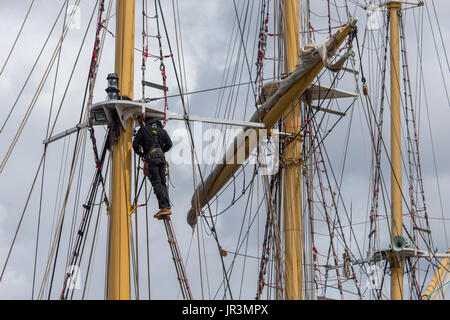 Ein Seemann auf ein Segel-Schulschiff empor an rigging Reparaturen arbeiten Stockfoto