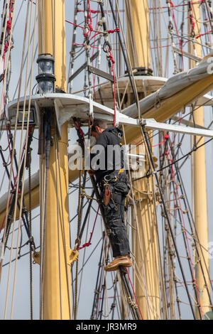 Ein Seemann auf ein Segel-Schulschiff empor an rigging Reparaturen arbeiten Stockfoto