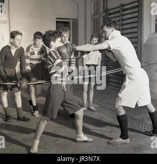 1948, England, einem jungen Schuljungen, der von einem männlichen Sportlehrer Verteidigung im Boxsport beigebracht wird, während andere Jungen sich anschauen und lernen, Hailleybury Public School, das einzige Internat eines traditionellen britischen Jungen. Stockfoto