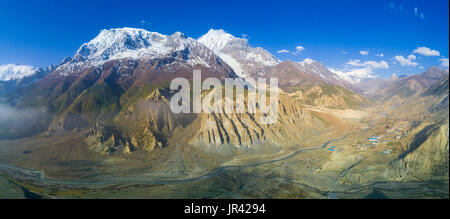 Großer Höhe geschwungenen Panorama der schneebedeckten Himalaya Annapurna Bergkette und Manang-Tal Dorf unten in Nepal Stockfoto