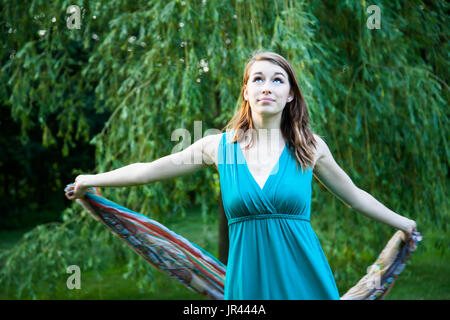 Schönes Mädchen dreht sich langsam um vor einer Weide. Unbeschwert, glücklich und froh in einem Park im Sommer. Stockfoto