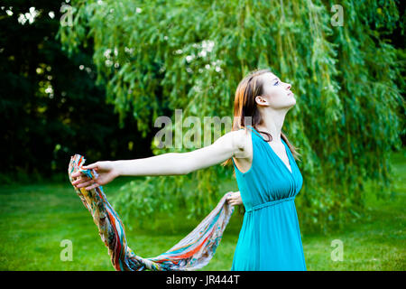 Schönes Mädchen dreht sich langsam um vor einer Weide. Unbeschwert, glücklich und froh in einem Park im Sommer. Stockfoto