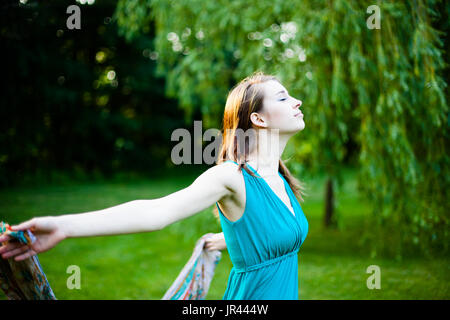 Schönes Mädchen dreht sich langsam um vor einer Weide. Unbeschwert, glücklich und froh in einem Park im Sommer. Stockfoto