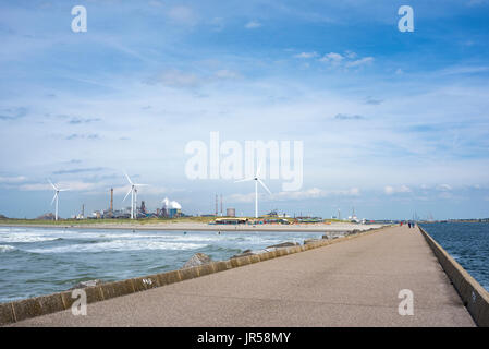 Dam an der Nordseeküste in der Nähe von Wijk aan Zee, an der Rückseite Windmühlen und das stahlwerk Tata, Ijmuiden, Nord Holland, Niederlande Stockfoto