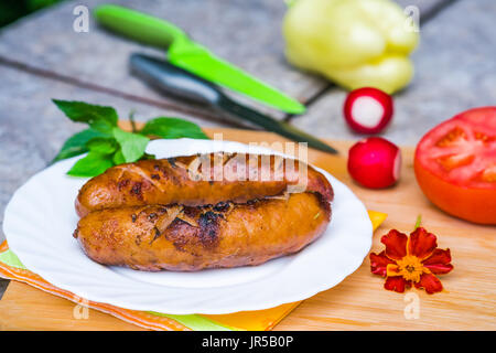 BBQ-Grillwurst auf einen Teller legen im Garten Stockfoto