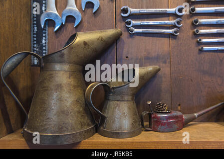 Öl kann groß und klein auf dem Tisch mit Schraubenschlüssel auf Holz Hintergrund Metall Stockfoto