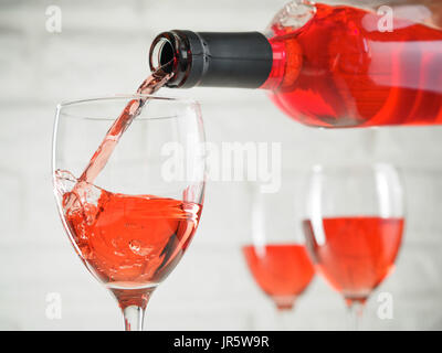 Gießen rosa Wein aus der Flasche in Weinglas auf weiße Ziegel Wand Hintergrund. Zwei Weinglas mit Roséwein auf Hintergrund. Kopieren Sie Raum. Stockfoto