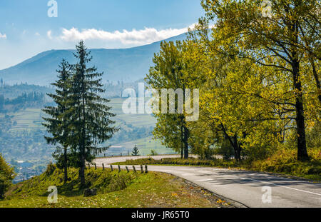 Wald entlang der Hügel Straße an einem sonnigen Tag. Serpentine auf Landschaft Tal mit großen Berg Hintergrund Stockfoto