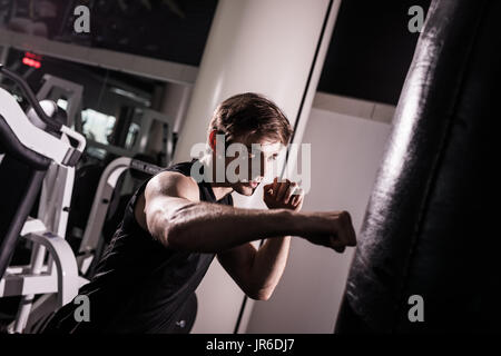 Junge Sportler trainieren durch das Werfen Schläge bei einem schweren Boxsack Stockfoto