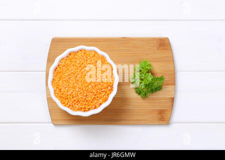 Schüssel mit geschälten roten Linsen auf Holzbrett Stockfoto