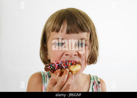 Porträt einer kleinen braunen behaartes Mädchen essen einen Donut mit bunten Streuseln Stockfoto