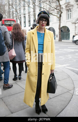 LONDON - Februar 18: Brünette Frau in einem Yelllow Mantel vor Somerset Haus während der London Fashion Week am 18. Februar 2014. London Fashionweek Stockfoto