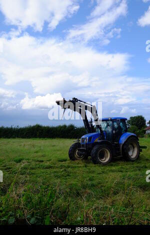 Ein Traktor mäht Rasen auf einer Farm in Lincolnshire, bleibt der Rasen um Heu zu machen. Stockfoto