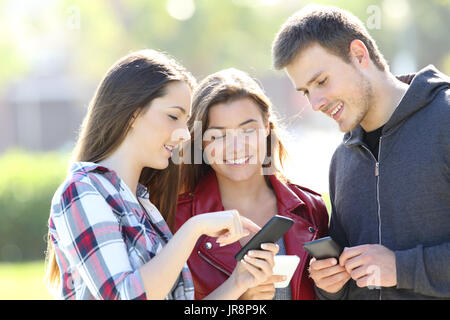 Drei Freunde stehen und den Austausch auf Linie mit ihren Smartphones auf der Straße Stockfoto