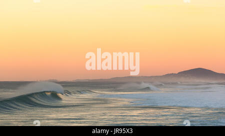 Brechende Welle bei Sonnenaufgang am Sunshine Beach, mit Mount Coolum im Hintergrund Stockfoto