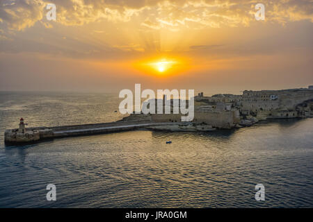 Sonnenuntergang im Hafen von Valletta Malta mit einem Leuchtturm und einsamen kleinen Boot im Mittelmeer Stockfoto