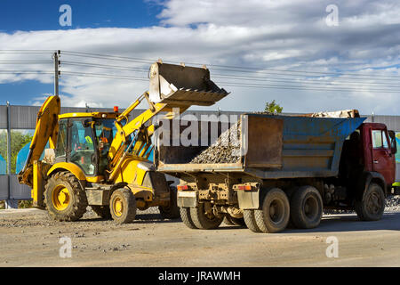 Schweren Traktor lasten Lkw mit Schutt mit Schaufel. Bau der Umgehungsstraße um Krassnoje Selo, Sankt Petersburg. Schwere industrielle Mac Stockfoto