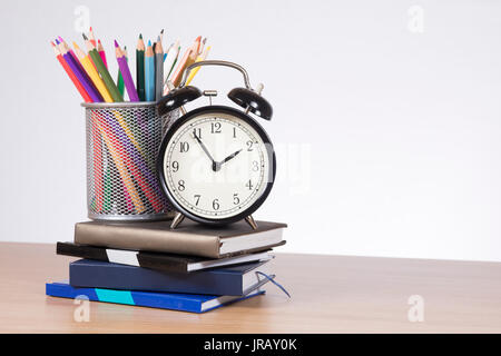 Buntstifte in Halter und Wecker steht auf Stapel von Notebooks Stockfoto