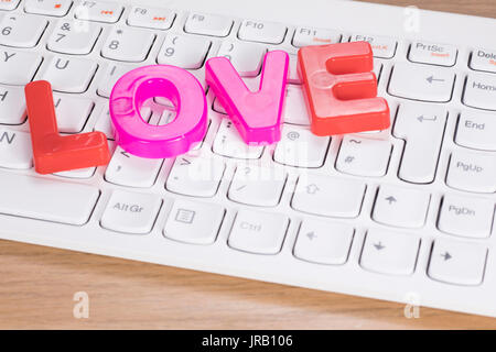 Das Wort Liebe aus Kunststoff Spielzeug Buchstaben über die Tastatur auf dem Schreibtisch, close-up hohen Winkel Konzept Stockfoto