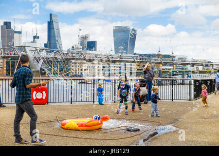 Straße Entertainer Hereinholen Tipps unterhalten Kinder durch Einblasen große bunte Luftblasen, Bankside, Böschung, South Bank, London SE1, UK Stockfoto