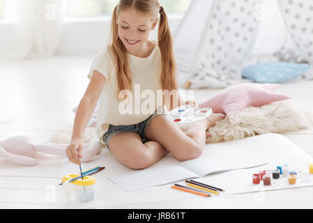 Talentierte Mädchen sitzt auf dem Boden und Waschbürsten beim Malen Stockfoto