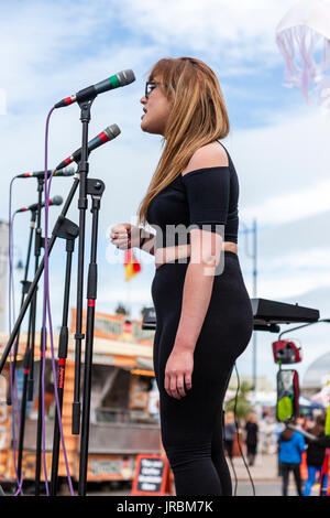 Junge kaukasier blonde Frau mit Brille stehen auf der Bühne singen. Dannli Jayne, Singer Song Writer führt bei eh Ramsgate festival Open Air Bühne. Stockfoto