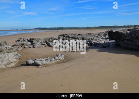 Ebbe auf ogmore Strand mit dem Dorf Newton im Hintergrund und ein paar Spaziergänger und ihre Hunde. Die niedrige tideleaves viel Rock Pools. Stockfoto