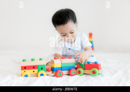 Entzückende asiatische Baby junge 9 Monate am Bett sitzen und spielen mit Farbe Holzeisenbahn Spielzeug zu Hause.
