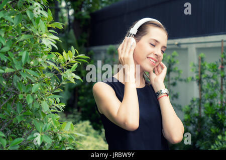 Schöne Russische Frau Musik hören, während Sie die Augen schließen, mit weißen Kopfhörer im Garten zu Hause. Entspannend. Stockfoto