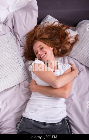 Junge rothaarige Frau lachend im Bett liegend Stockfoto