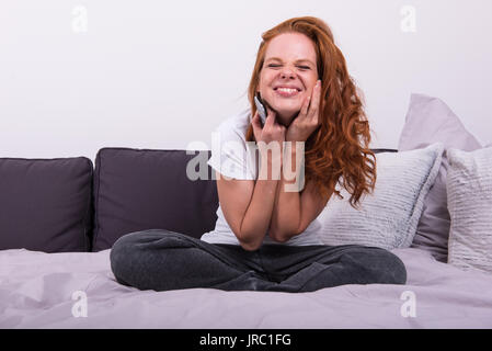 Junge rothaarige Frau mit der Fernbedienung in der Hand vor dem Fernseher Stockfoto