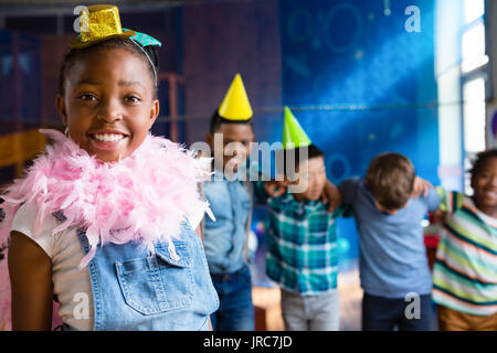 Portrait von Mädchen mit Feder Boa mit Freunden im Hintergrund während der Geburtstagsfeier Stockfoto