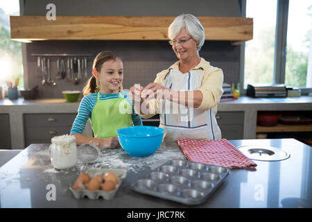 Lächelnde Großmutter, Enkelin Eier in der Küche zu brechen Stockfoto