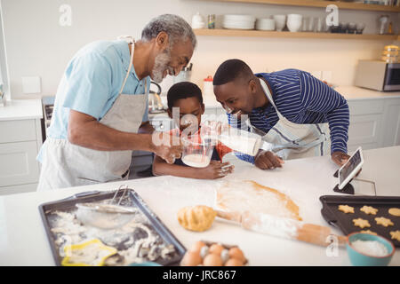 Multi-Generation gießen Milch in einem Glas während der Vorbereitung Cookies in der Küche Stockfoto
