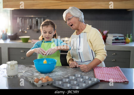 Enkelin Aufschlagen der Eier und Großmutter aufpassen beim Stehen in der Küche Stockfoto