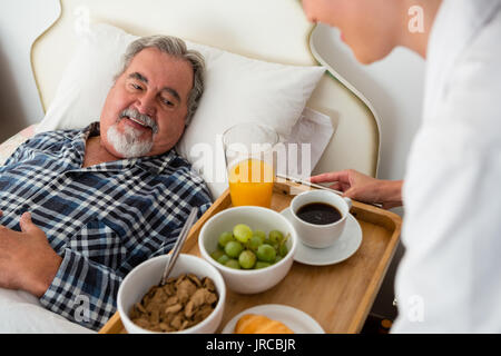 7/8 Hand der Ärztin mit Speisen zu den älteren Patienten entspannen auf Bett im Pflegeheim Stockfoto