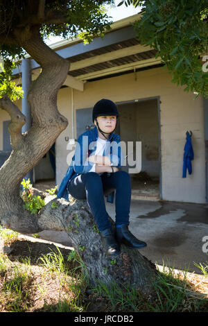 Nachdenkliches Mädchen sitzen auf Baumstamm in der Nähe von Stable Stockfoto