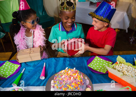 Hohe Betrachtungswinkel von Freunden Geschenke zu geben, Junge beim am Tisch während der Geburtstagsfeier sitzen Stockfoto