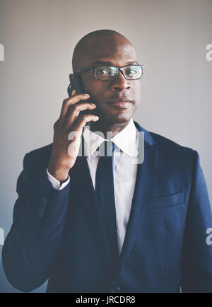 Porträt einer selbstbewussten jungen afrikanischen Geschäftsmann in Anzug und Brille Gespräche am Mobiltelefon, während allein in einem Büro Stockfoto