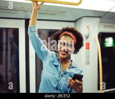 Stilvolle Junge afrikanische Frau lächelnd und hören die Musik auf Ihr Handy während der Fahrt mit der U-Bahn während Ihrer täglichen Pendeln Stockfoto