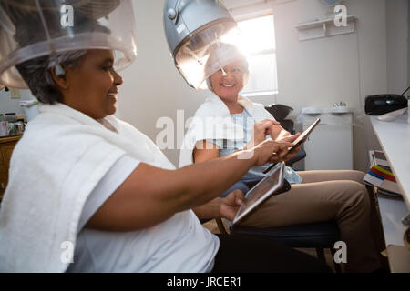 Freunde mit digitalen Tablet während unter Haar Dampfgarer, die im Salon sitzen Stockfoto