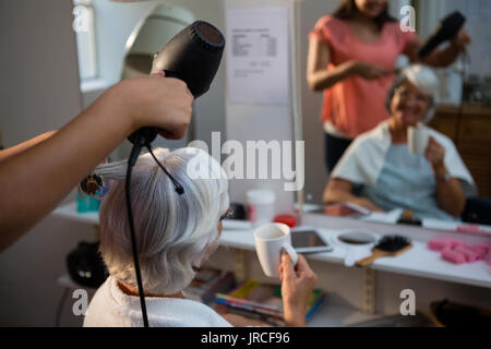 Kosmetikerin trocknen Senior Frau Haar auf Spiegel im Salon widerspiegelt Stockfoto