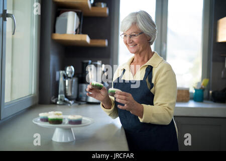 Ältere Frau herauf die Cupcake aus dem Fach in der Küche Stockfoto