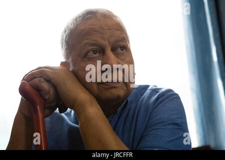 Nachdenklich älterer Mann mit Spazierstock, während durch die Fenster in der Krankenpflege zu Hause sitzen Stockfoto